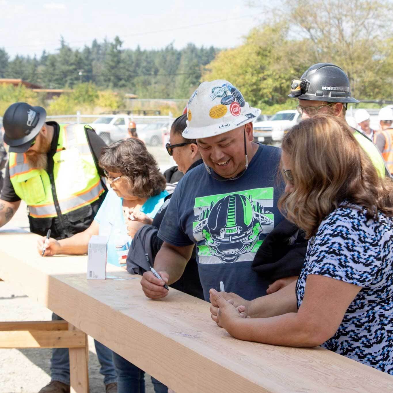Employees signing a wooden beam at a construction site.