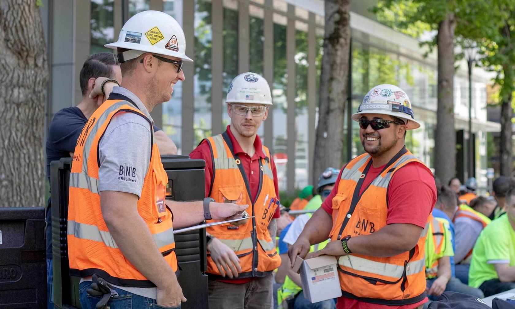 BNBuilders employees wearing hardhats and safety vests talking in a group.